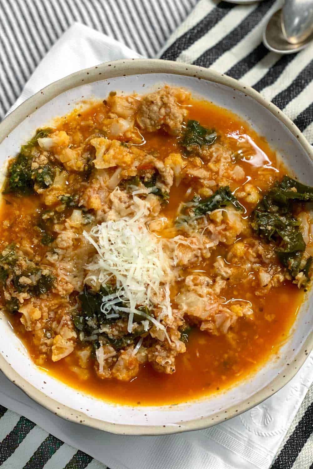 overhead shot of a white bowl filled with ground turkey vegetable soup and a heap of shredded parmesan in the middle.