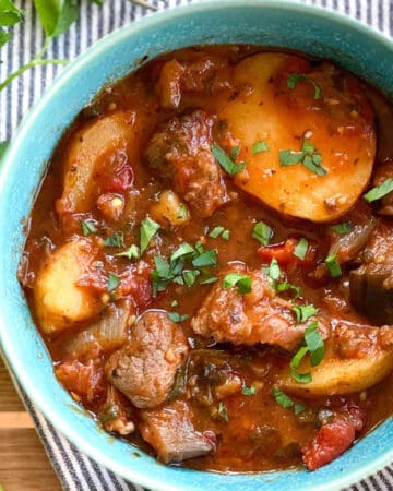 Lamb stew with potatoes in a blue china bowl topped with chopped parsley.