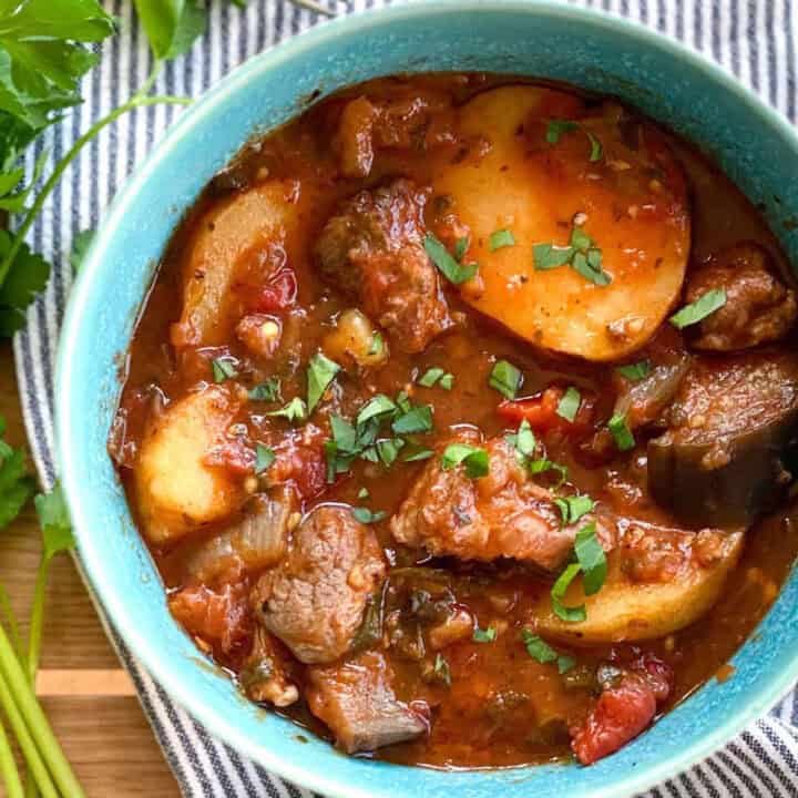 Lamb stew with potatoes in a blue china bowl topped with chopped parsley.