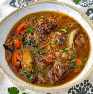 overhead shot of a white bowl filled with beef bourguignon, on a black and white flowered cloth napkin with four forks