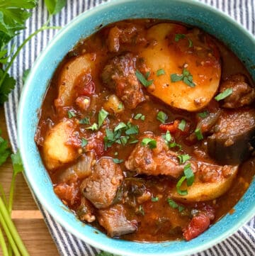 Georgian lamb stew with potatoes in an aqua bowl on a striped dish cloth with 5 forks in the background