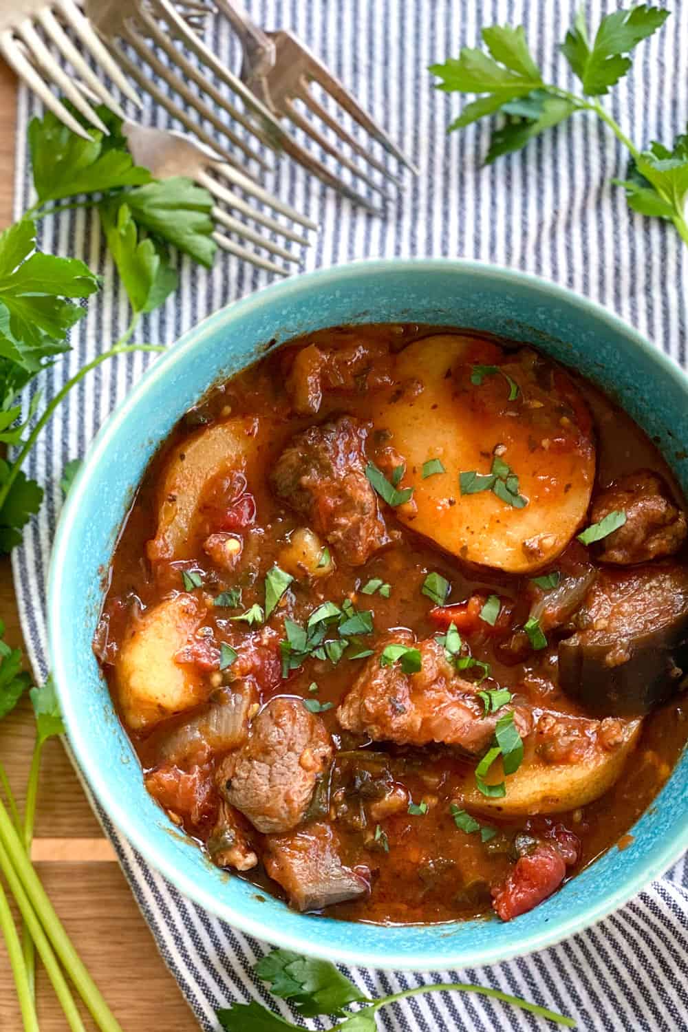 Georgian lamb stew with potatoes in an aqua bowl on a striped dish cloth with 5 forks in the background