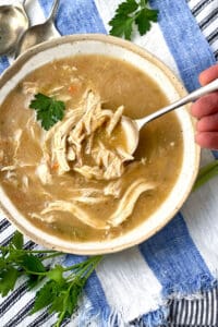 Creamy chicken soup with lots of shredded chicken in a white bowl with a leaf of parsley and a spoon