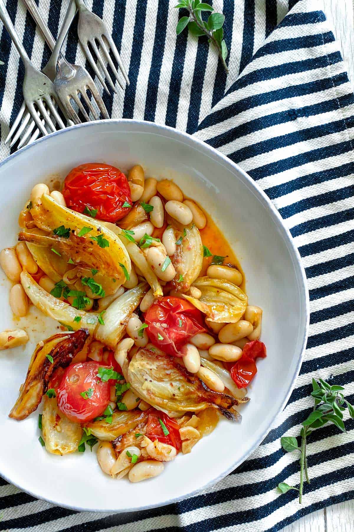 white bowl on a black and white striped dish towel, filled with roasted fennel, cherry tomatoes and white beans