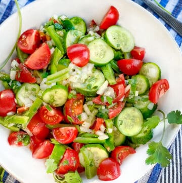 A white bowl filled with Shirazi salad of cucumbers cherry tomatoes green peppers and onions