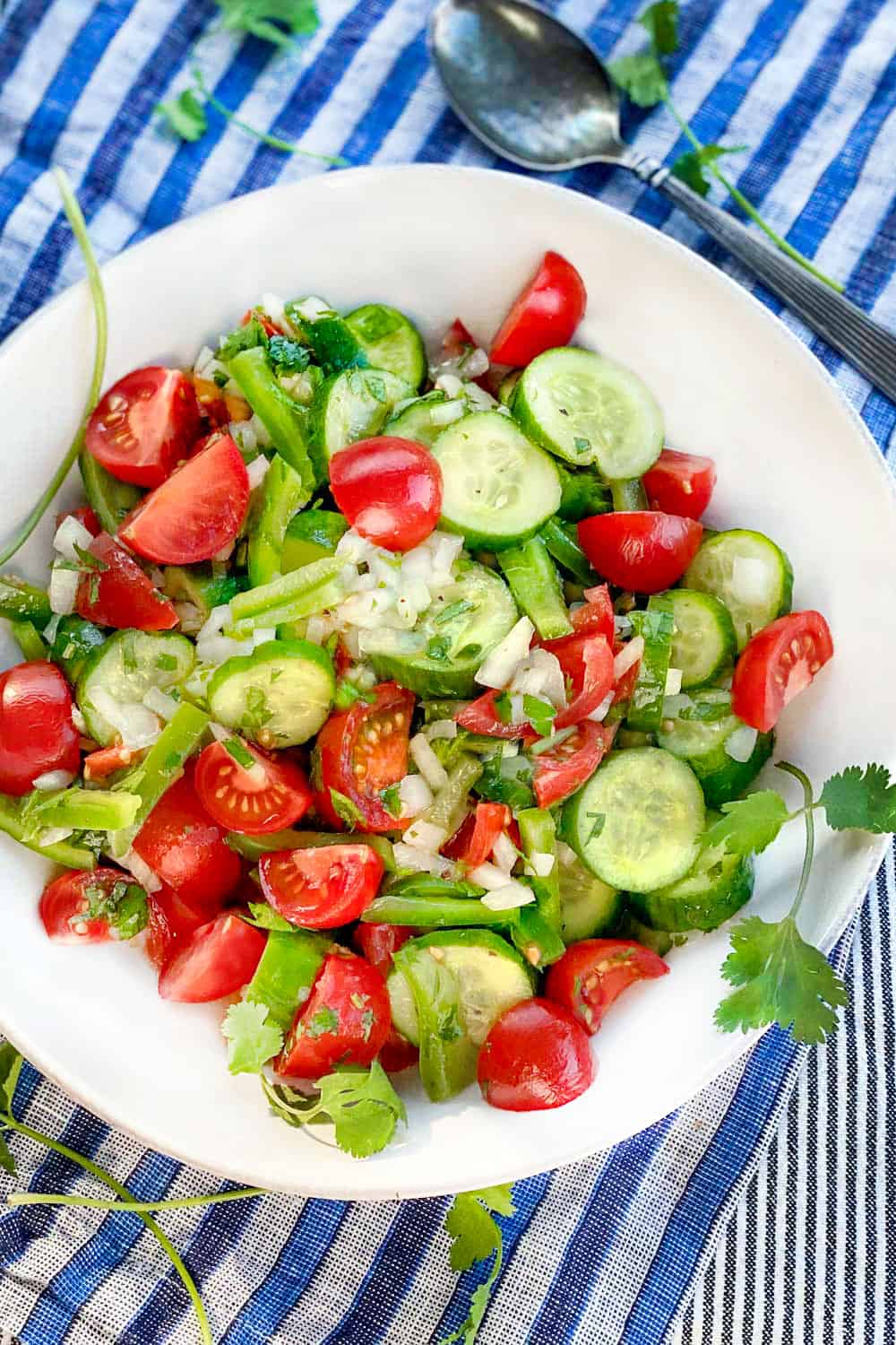 A white bowl filled with Shirazi salad of cucumbers cherry tomatoes green peppers and onions