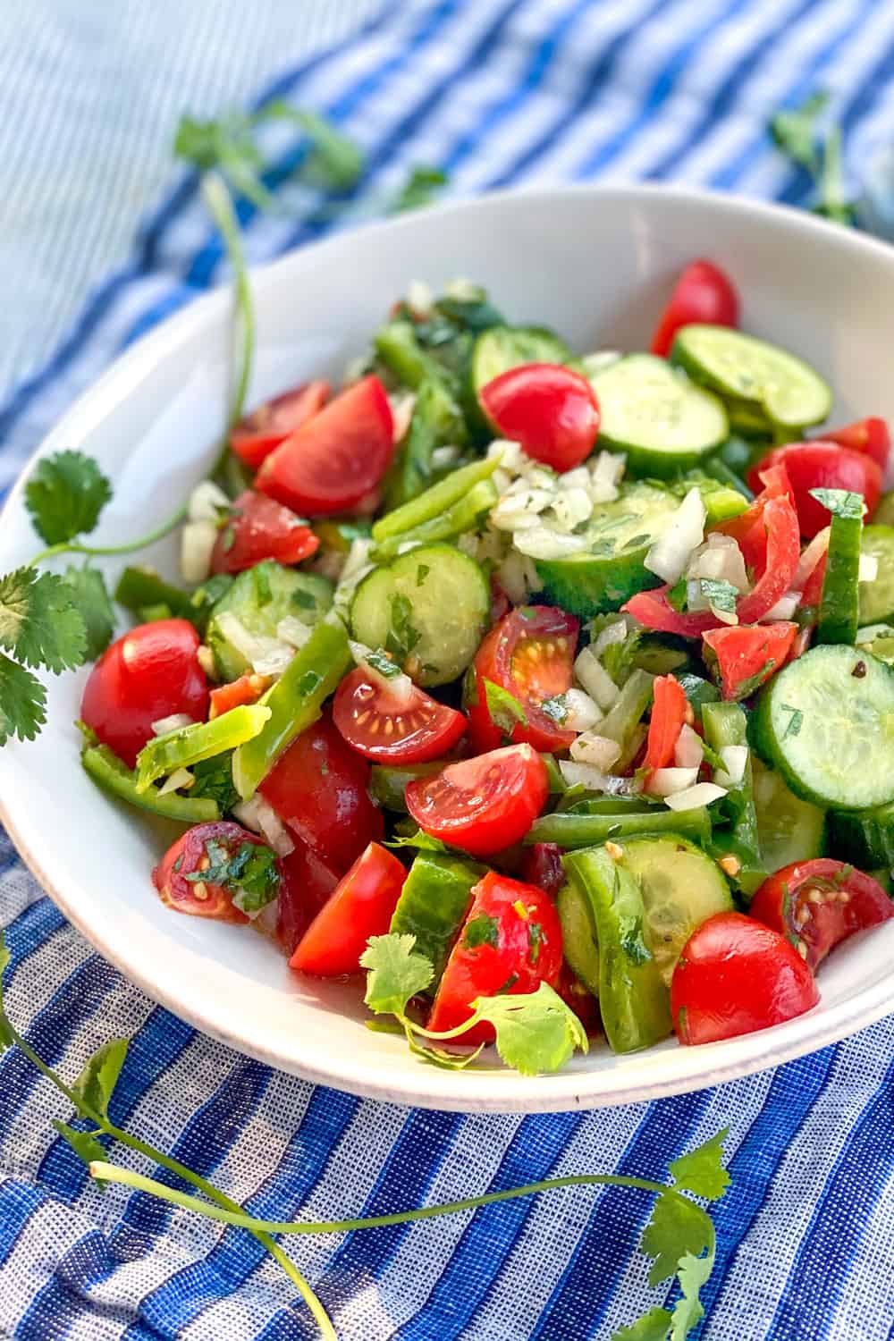 A white bowl filled with Shirazi salad of cucumbers cherry tomatoes green peppers and onions