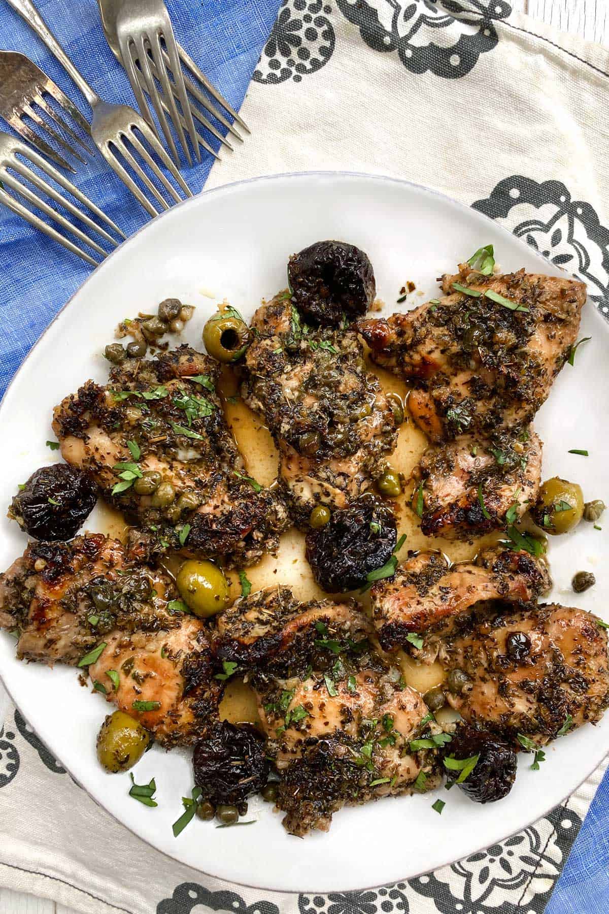 6 pieces of boneless chicken marbella with prunes and olives, on a white plate, with 5 forks in the background