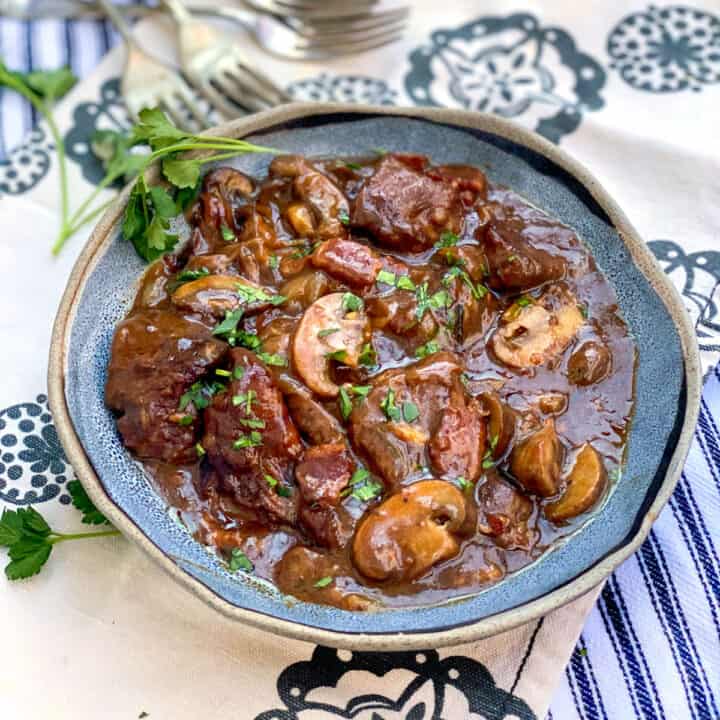 beef bourguignon in a blue bowl garnished with a sprig of parsley.