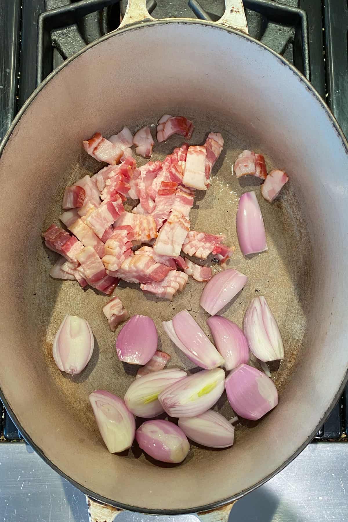 shallots and bacon cubes in an oval dutch oven.
