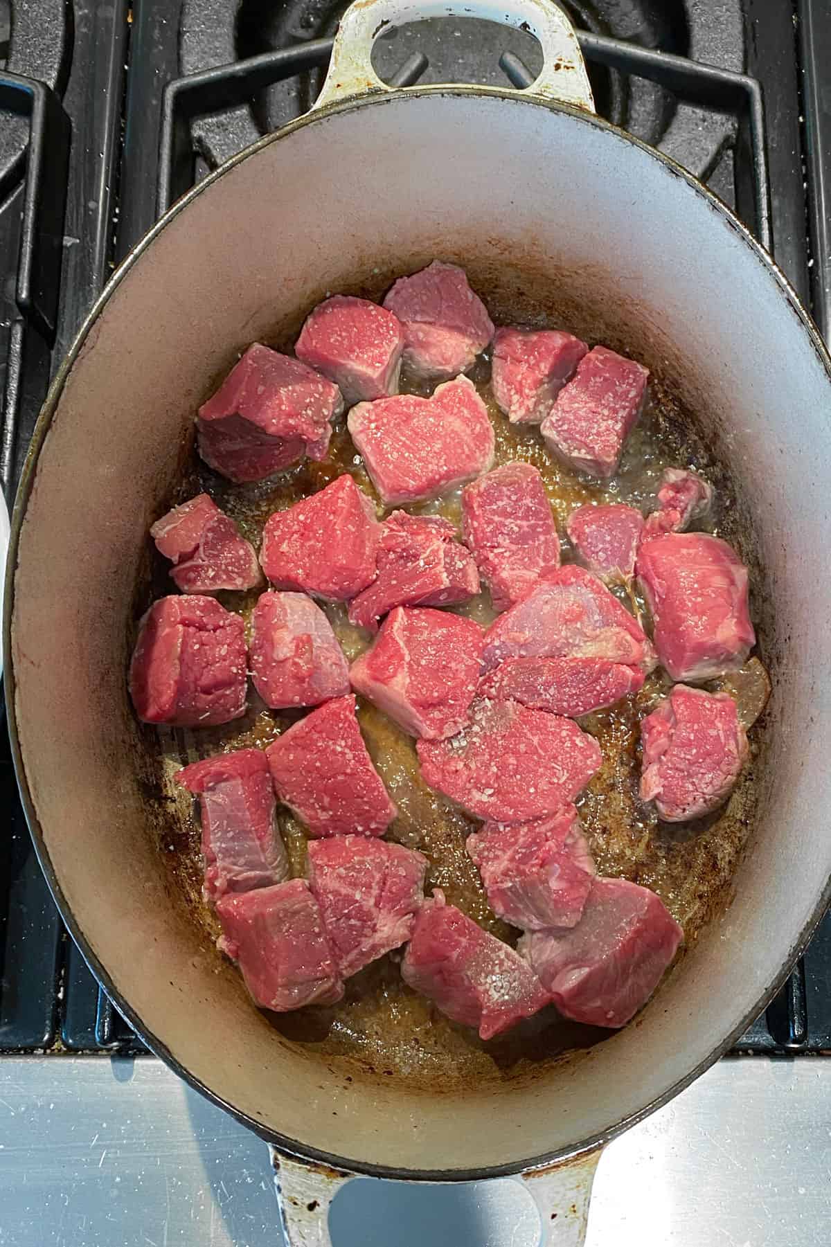 beef cubes sautéing in an oval dutch oven.