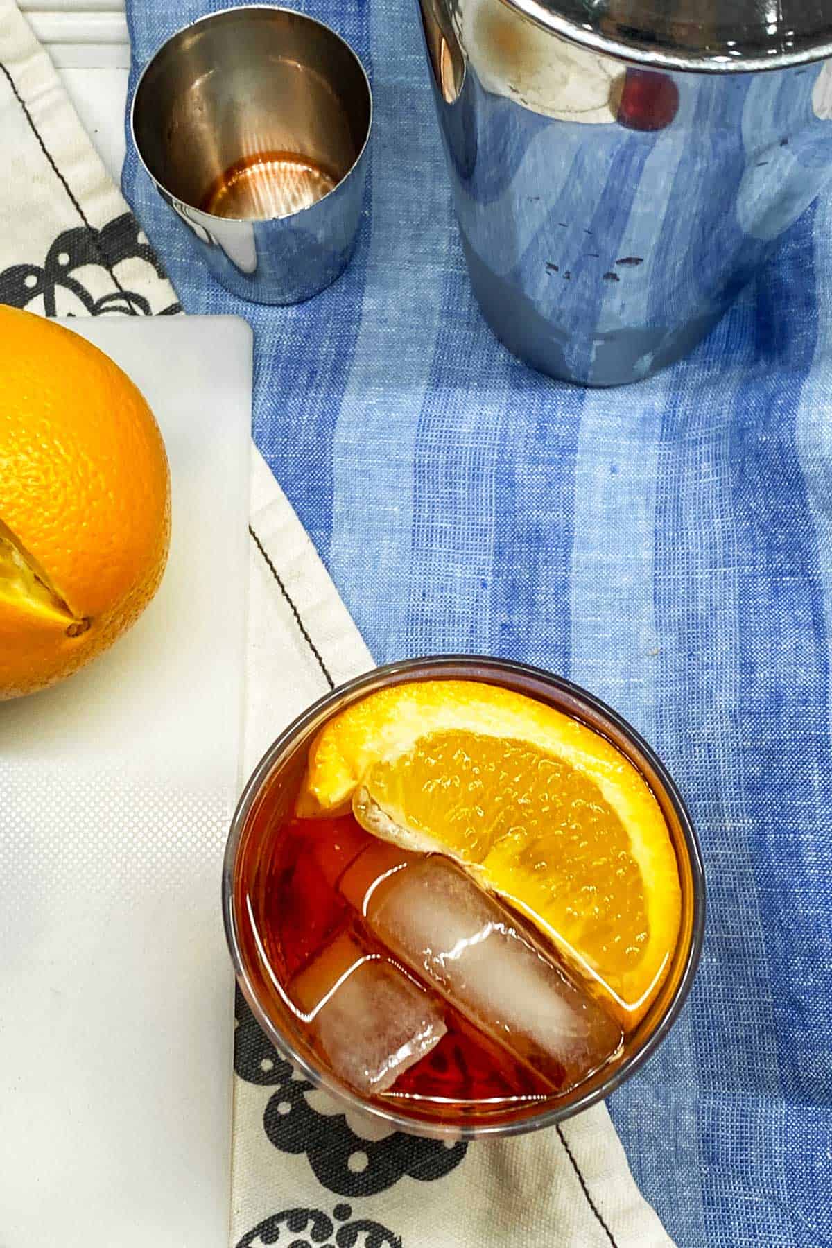 looking down into a negroni cocktail with ice and an orange slice, on a blue dish towel 