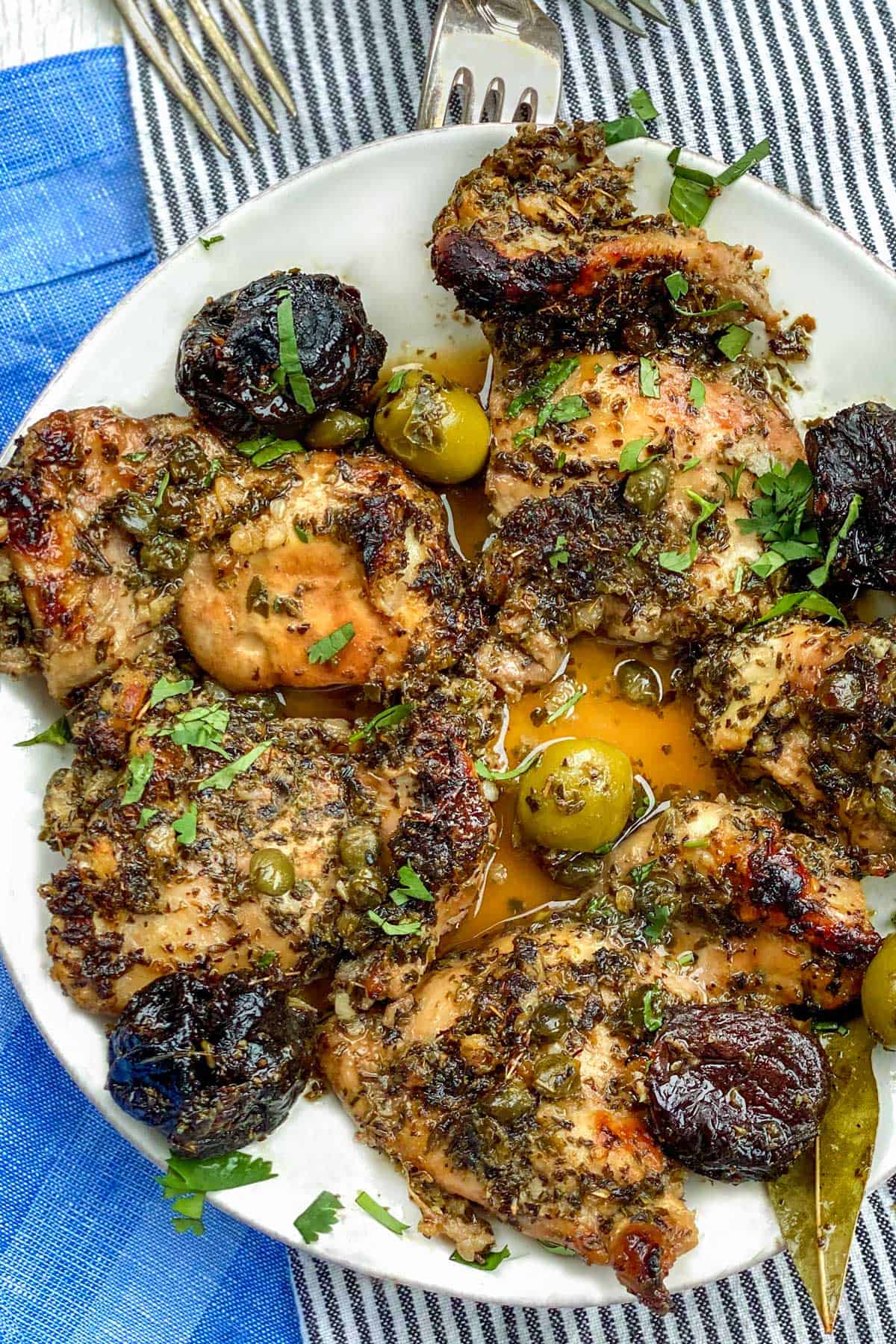 Close up of a plate with 5 pieces of boneless chicken marbella, a few prunes and green olives and a garnish of chopped parsley