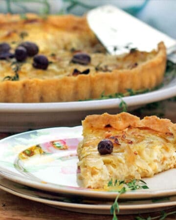A slice of french onion tart on a fancy china appetizer plate with the rest of the tart in the background.