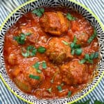 black and white decorative bowl filled with 6 Moroccan meatballs in tomato sauce, with chopped parsley sprinkled on top and a few forks in the background