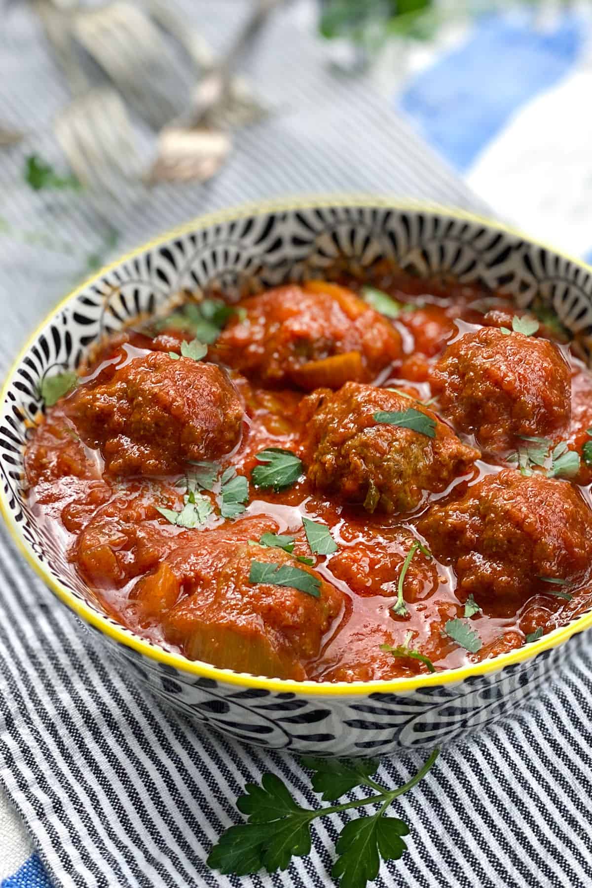 6 meatballs in a bowl with tomato sauce, a few forks in the background
