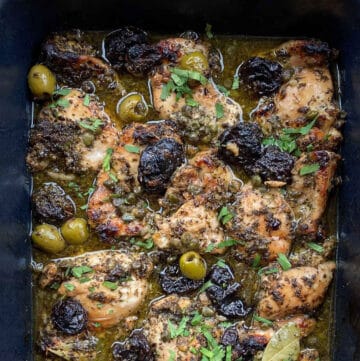 chicken Marbella in a roasting pan with prunes, green olives and a garnish of chopped parsley