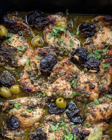 chicken Marbella in a roasting pan with prunes, green olives and a garnish of chopped parsley