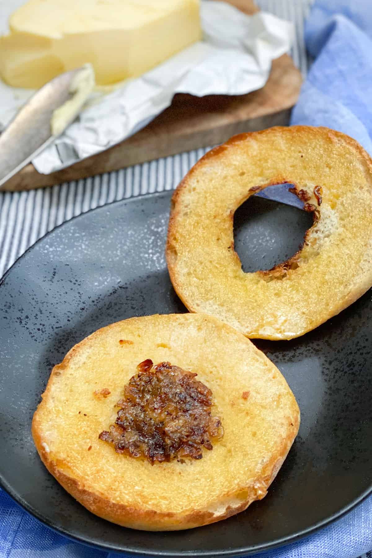 A sliced buttered bialy on a black plate with a bar of butter in the background