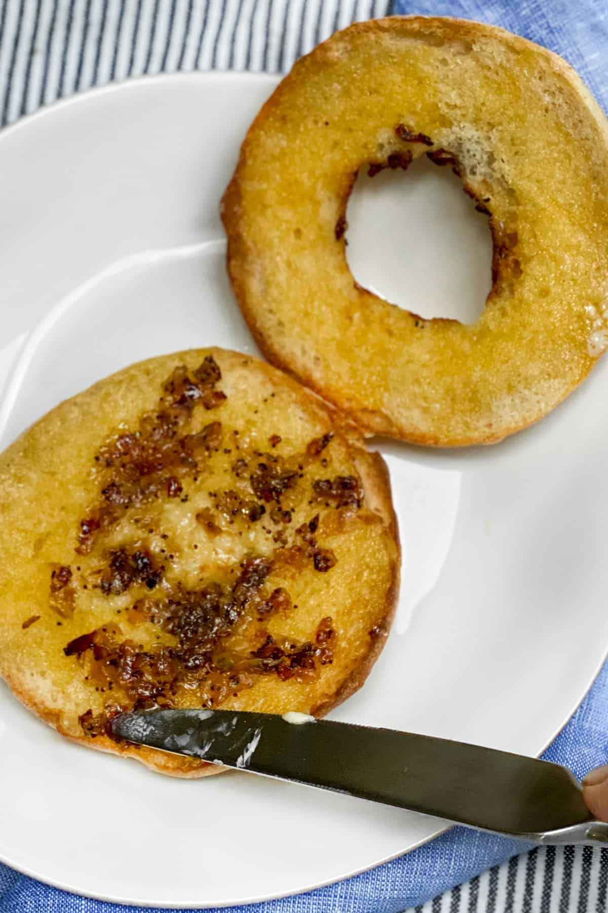 sliced bialy on a white plate being buttered, onions spread around