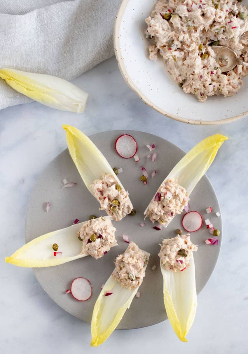 5 endive spears with tuna salad on the ends, sitting on a gray plate garnished with a few slices of radish and sprinkles of chopped red onion