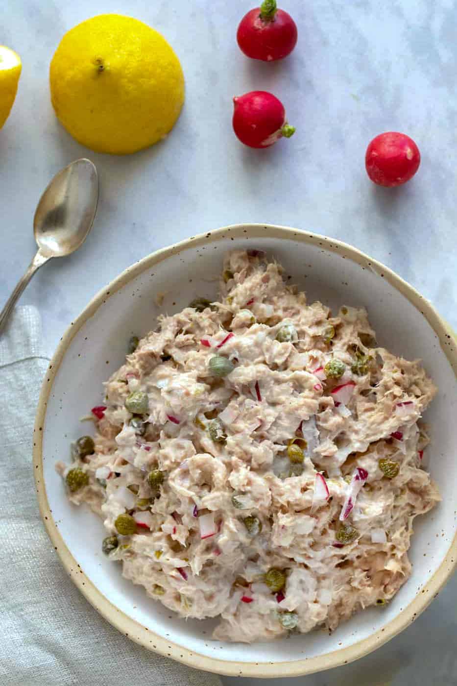 white bowl filled with tuna salad, 3 radishes and a half lemon in the background