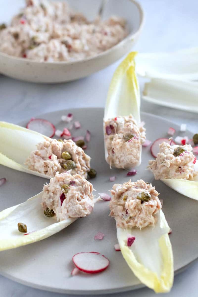 5 endive spears with tuna salad on the ends, sitting on a gray plate garnished with a few slices of radish and sprinkles of chopped red onion