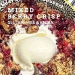 Berry crisp in a dessert bowl with a scoop of vanilla ice cream and a spoon.