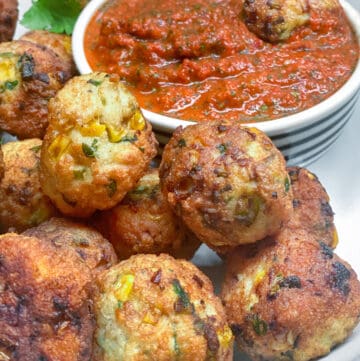 a pile of turkey corn meatballs on a white plate with a small bowl of red pepper dipping sauce in the background