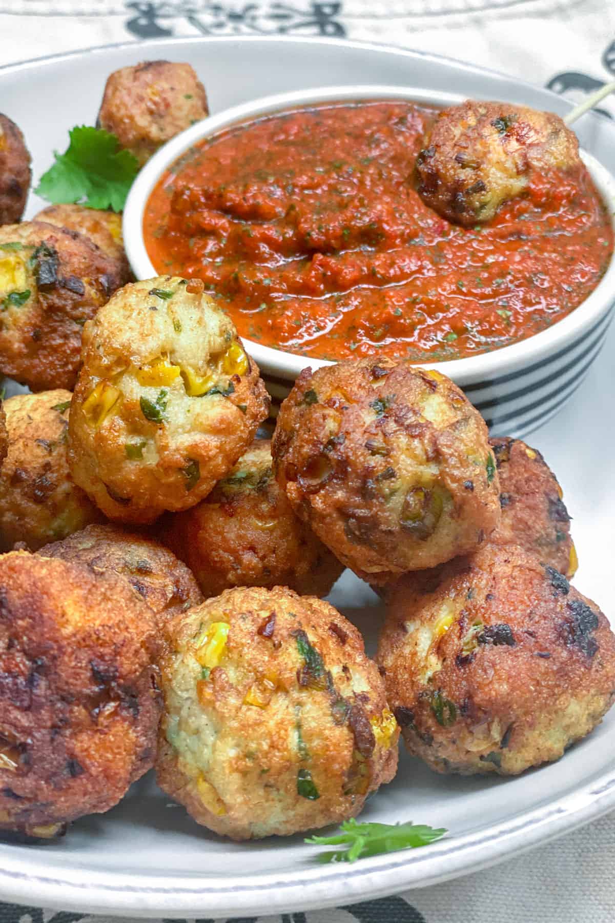 a pile of turkey corn meatballs on a white plate with a small bowl of red pepper dipping sauce in the background