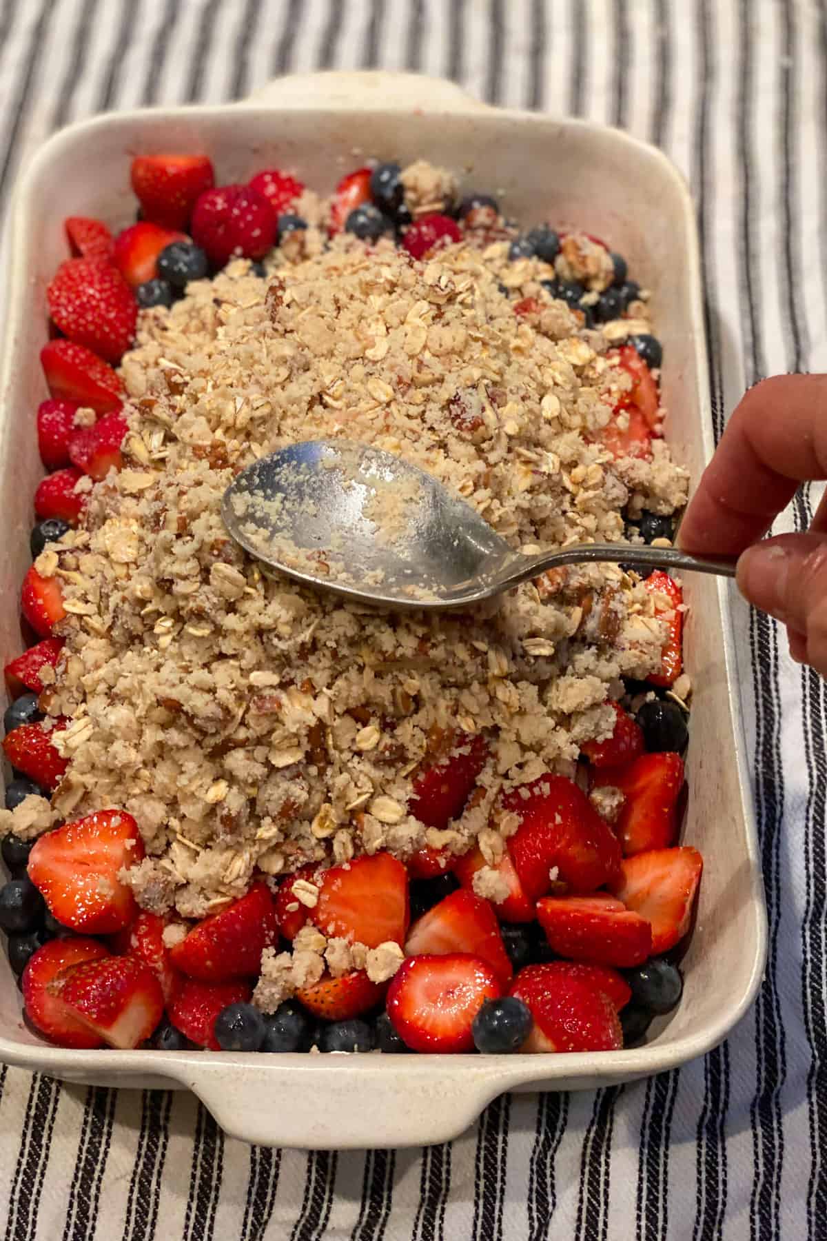 spreading the almond flour and pecan topping over the berries in the baking pan.