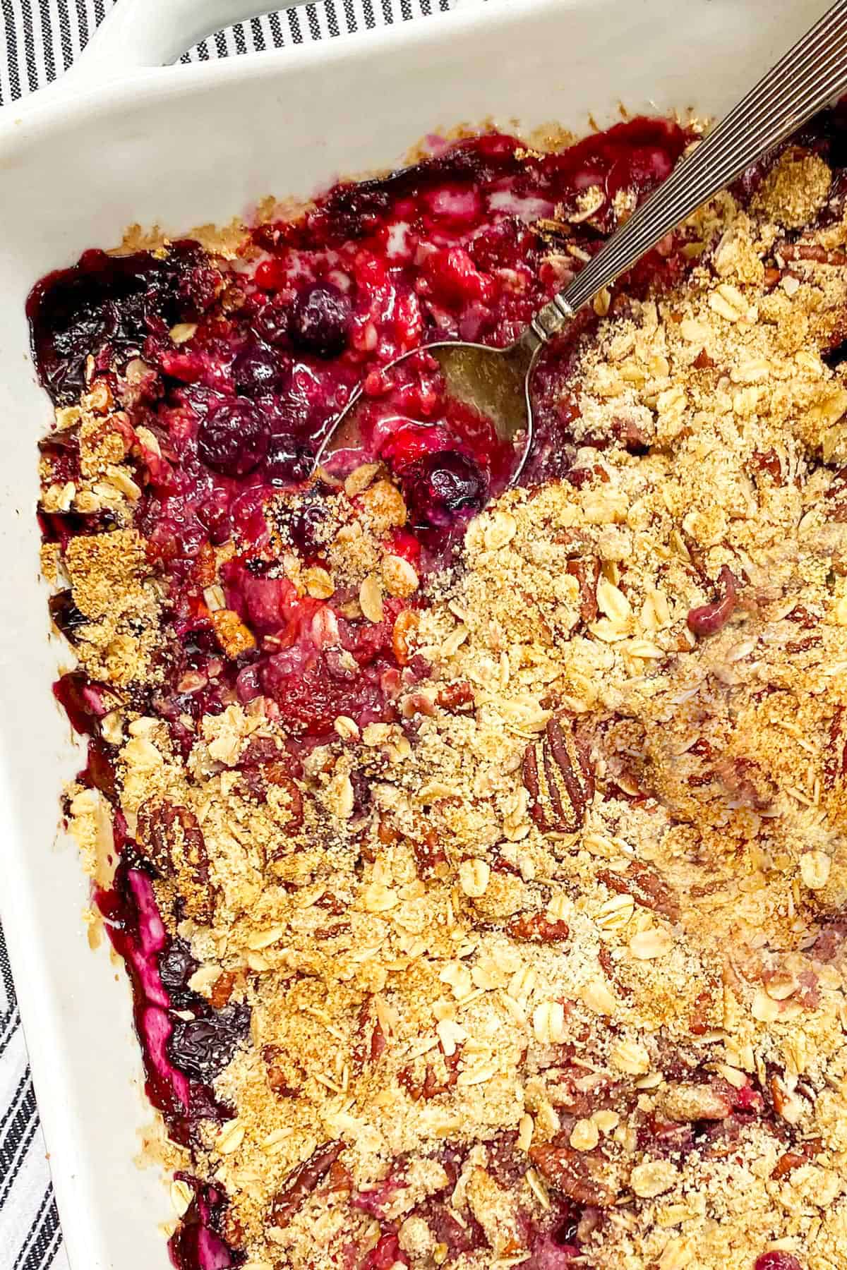Baked mixed berry crisp in a baking pan with a spoon scooping some out.