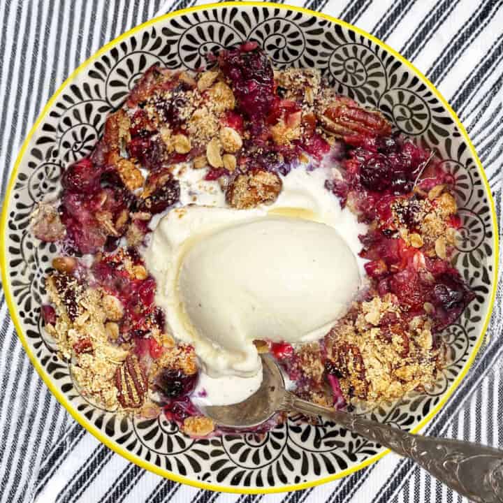 Berry crisp in a dessert bowl with a scoop of vanilla ice cream and a spoon.