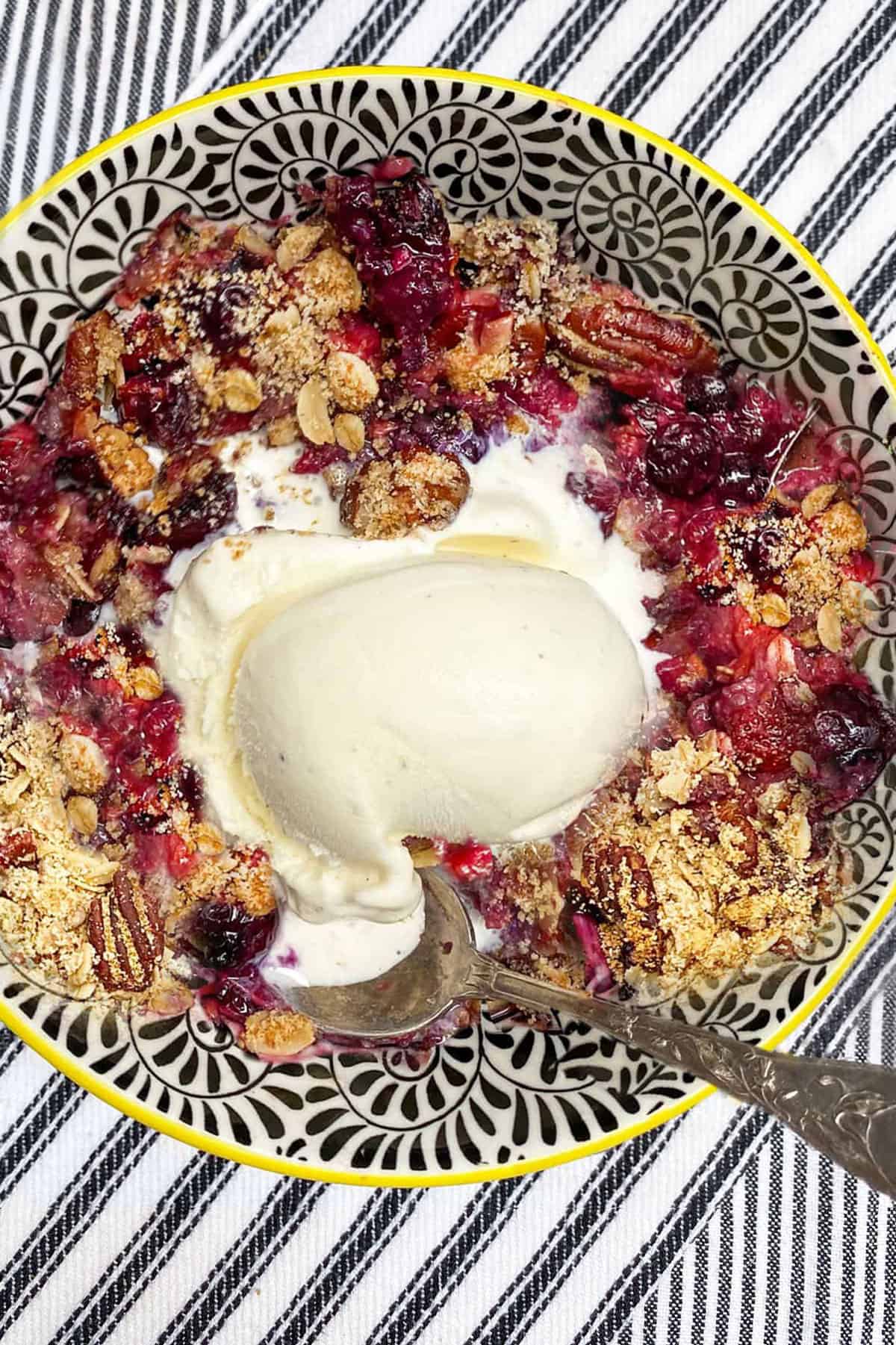 mixed berry crisp in a bowl with a scoop of vanilla ice cream and a spoon.