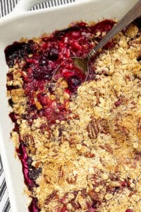 close up of a white baking pan filled with a mixed berry crumble, a spoon sticking out of the fruit