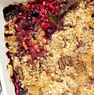 close up of a white baking pan filled with a mixed berry crumble, a spoon sticking out of the fruit