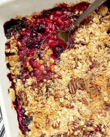 close up of a white baking pan filled with a mixed berry crumble, a spoon sticking out of the fruit