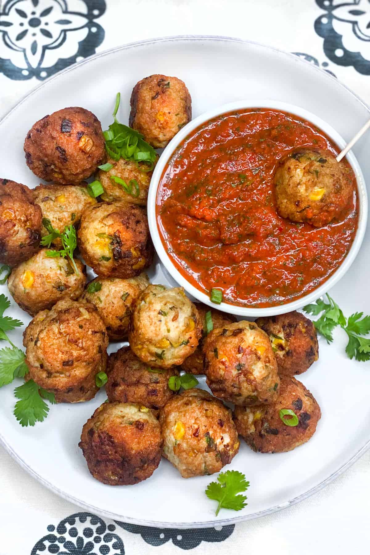 16 turkey corn meatballs on a plate surrounding a small bowl of roasted red pepper sauce, with one meatballs on a toothpick, resting in the sauce