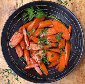sautéed carrot wedges in a black bowl, sprinkled with parsley