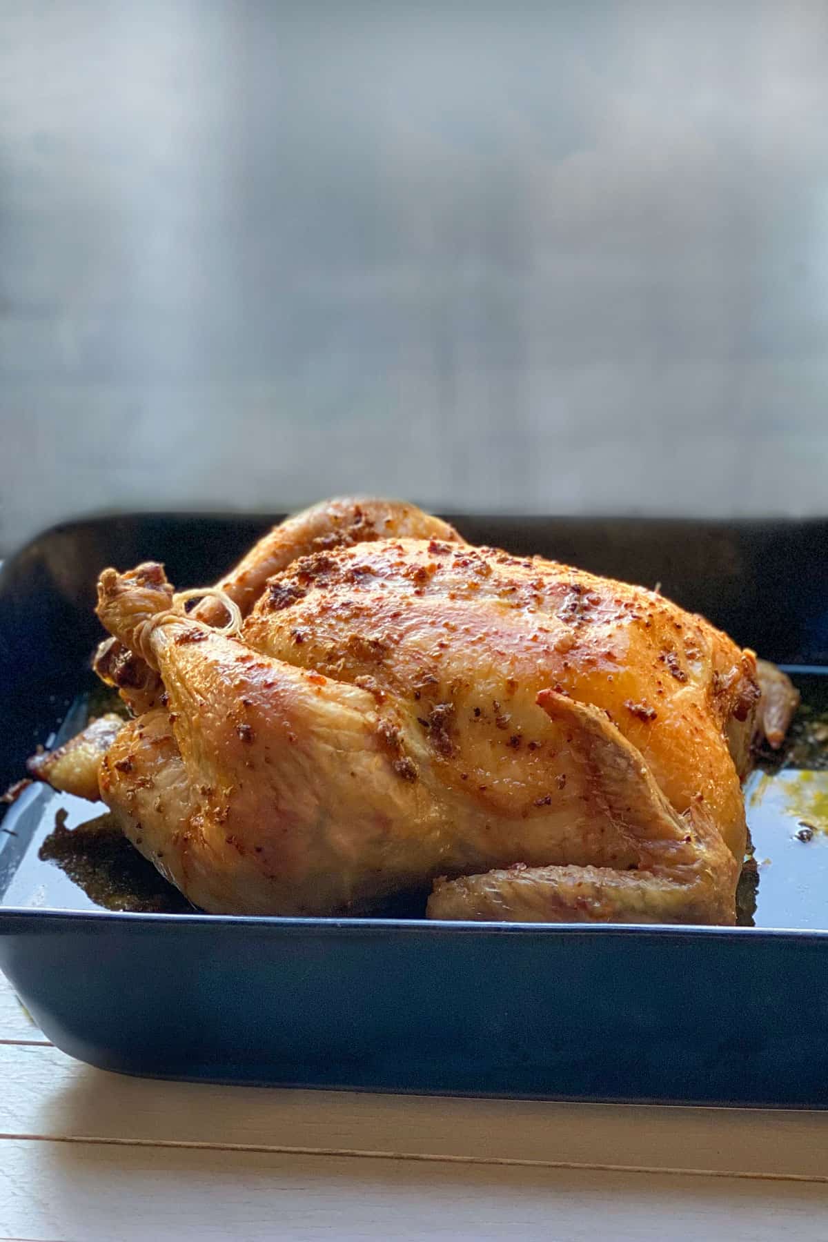 a whole slow roasted chicken in a black roasting pan, seen from the side