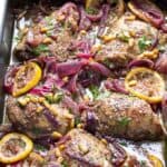 chicken thighs in a roasting pan with lemons, red onions and toasted pine nuts
