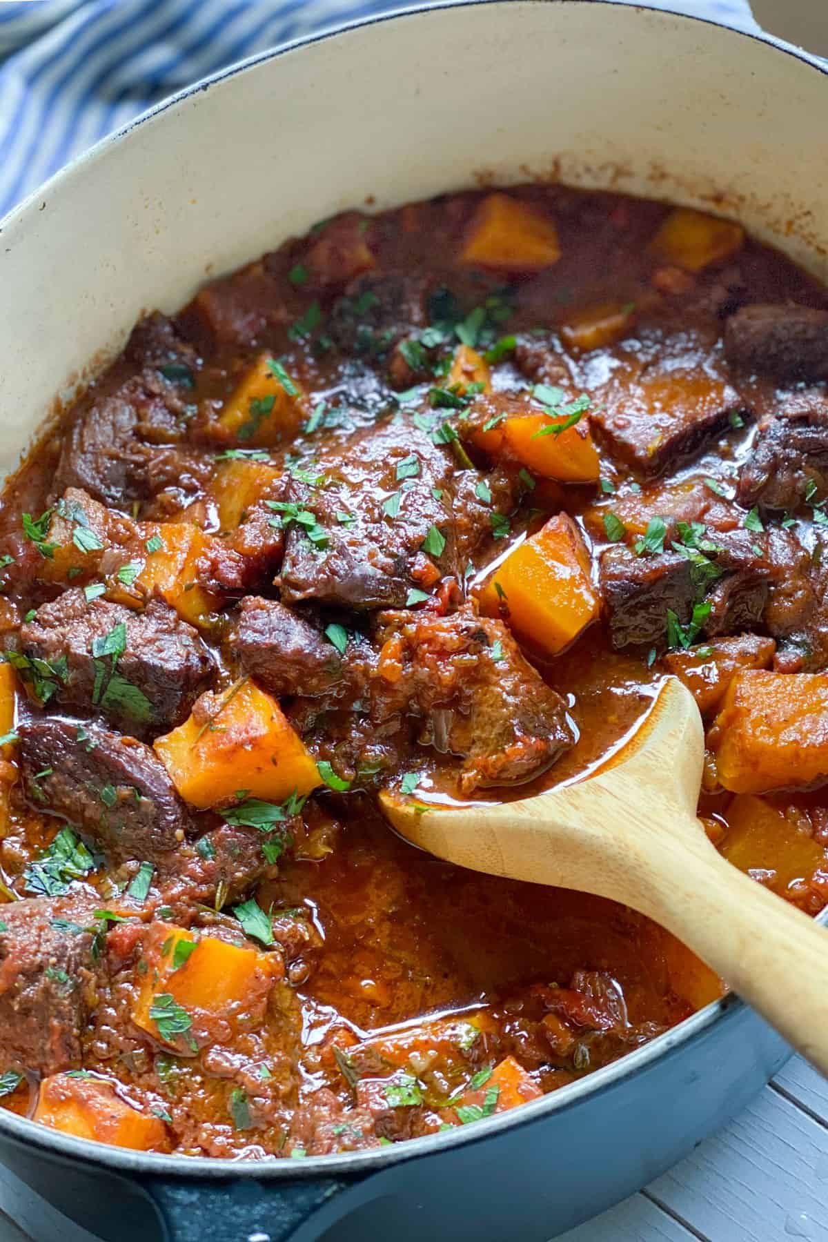 A dutch oven filled with a stew of beef short ribs and cubed butternut squash