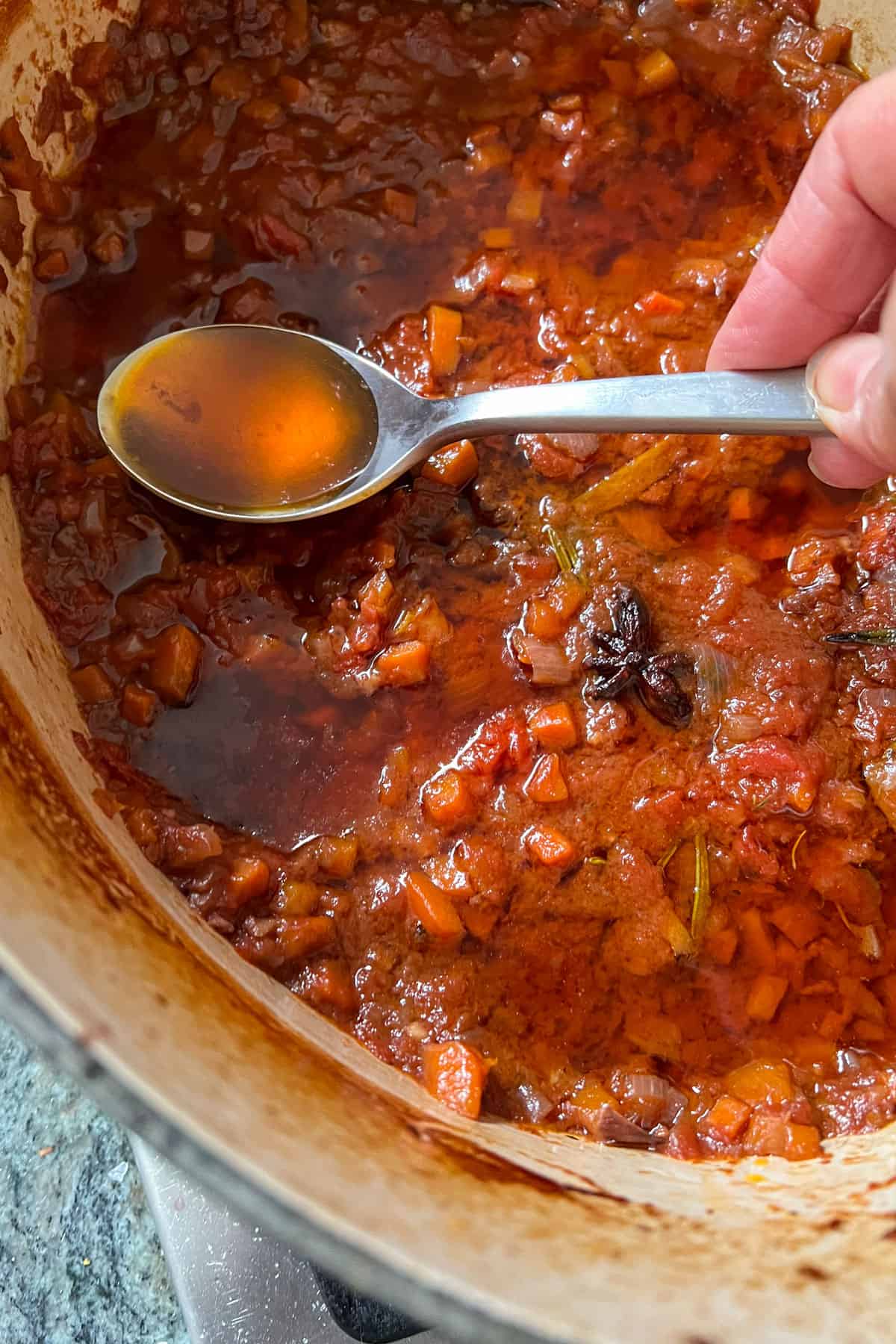 a spoon of orange-tinged fat held over a stew pot.