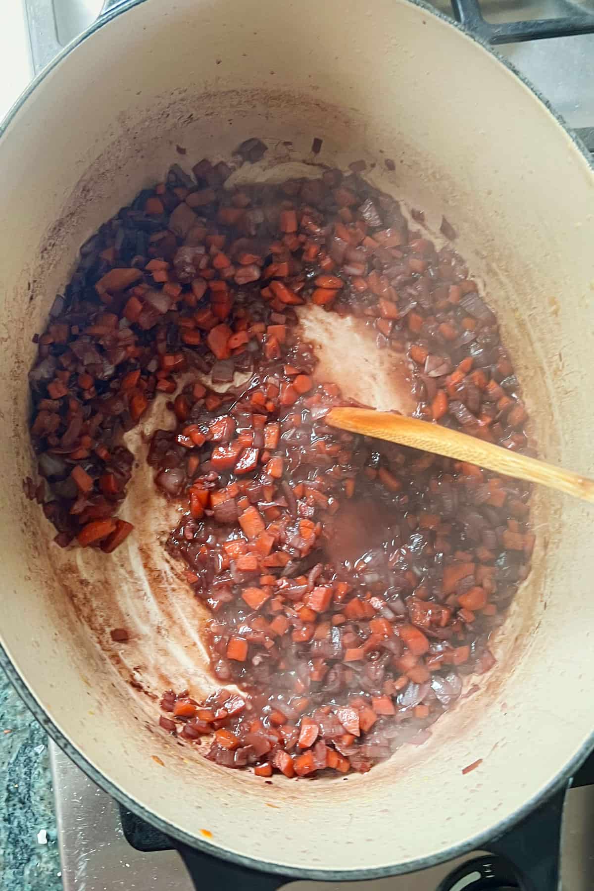 wooden spoon scraping the bottom of a dutch oven filled with aromatic vegetables and reduced wine.