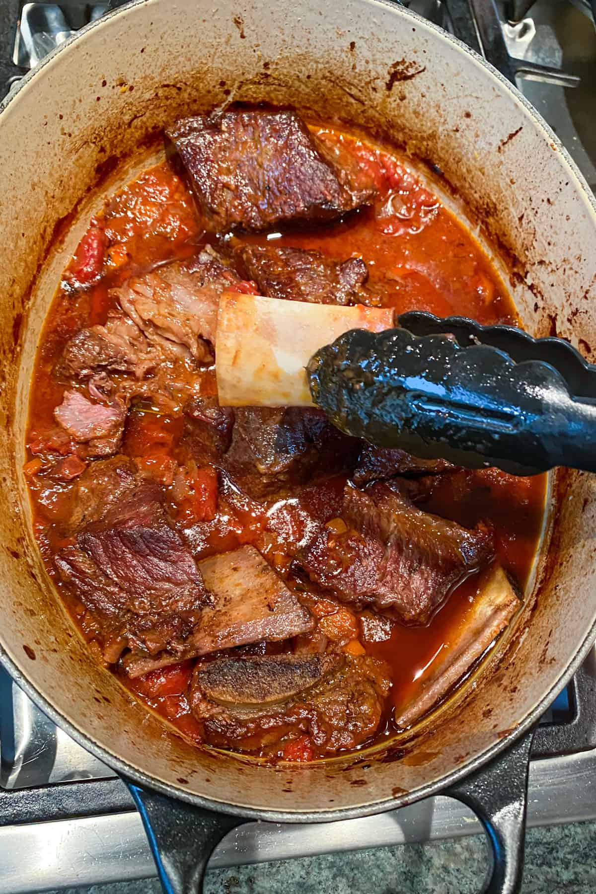 beef short rib stew out of the oven, tongs holding up a bone.