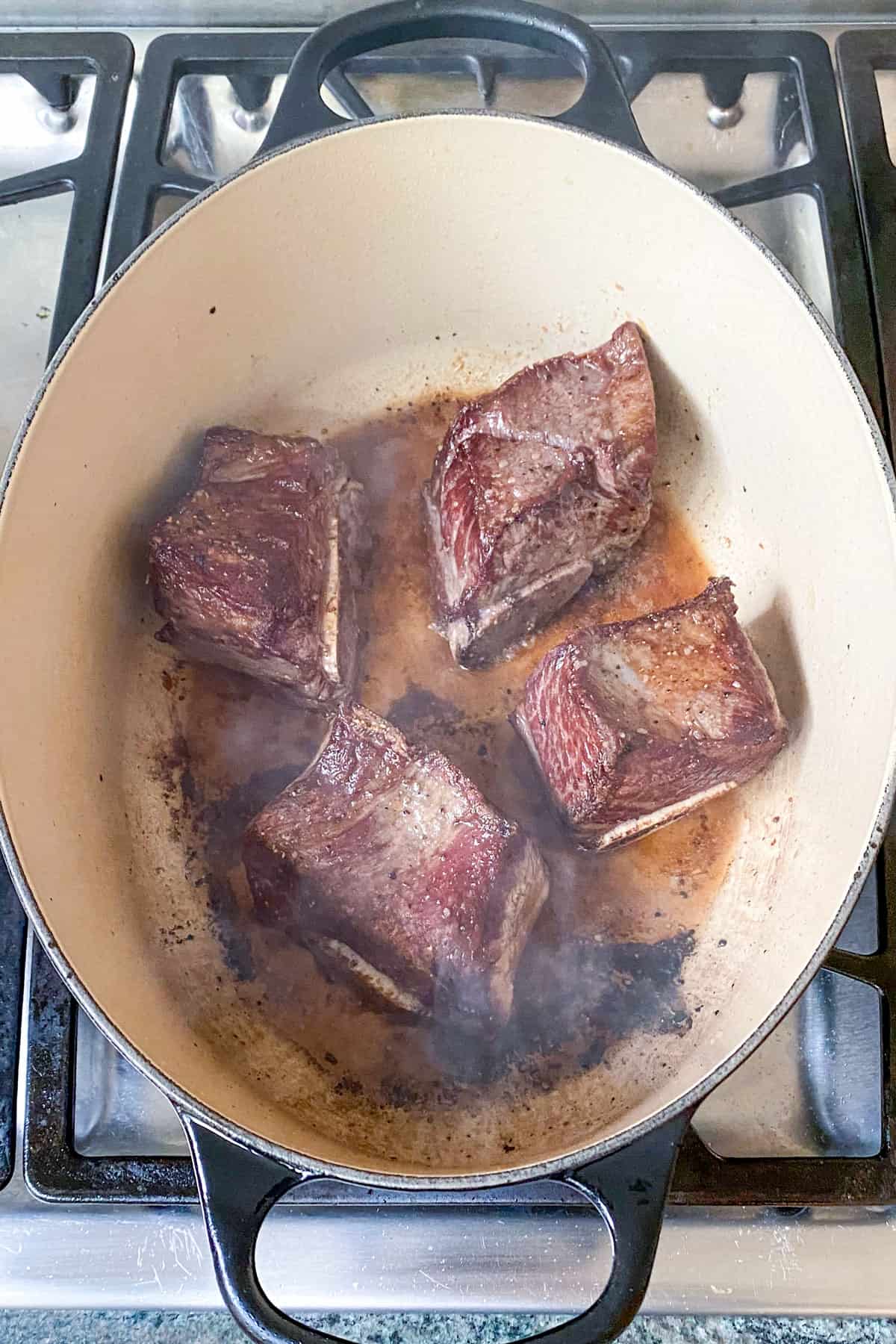 four seared short ribs in a dutch oven.