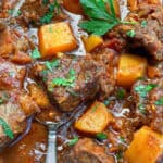 close up of beef short ribs and cubes of butternut squash in rich gravy with sprinkles of chopped parsley on top