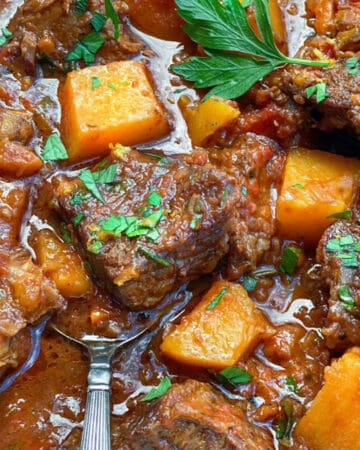 close up of beef short ribs and cubes of butternut squash in rich gravy with sprinkles of chopped parsley on top