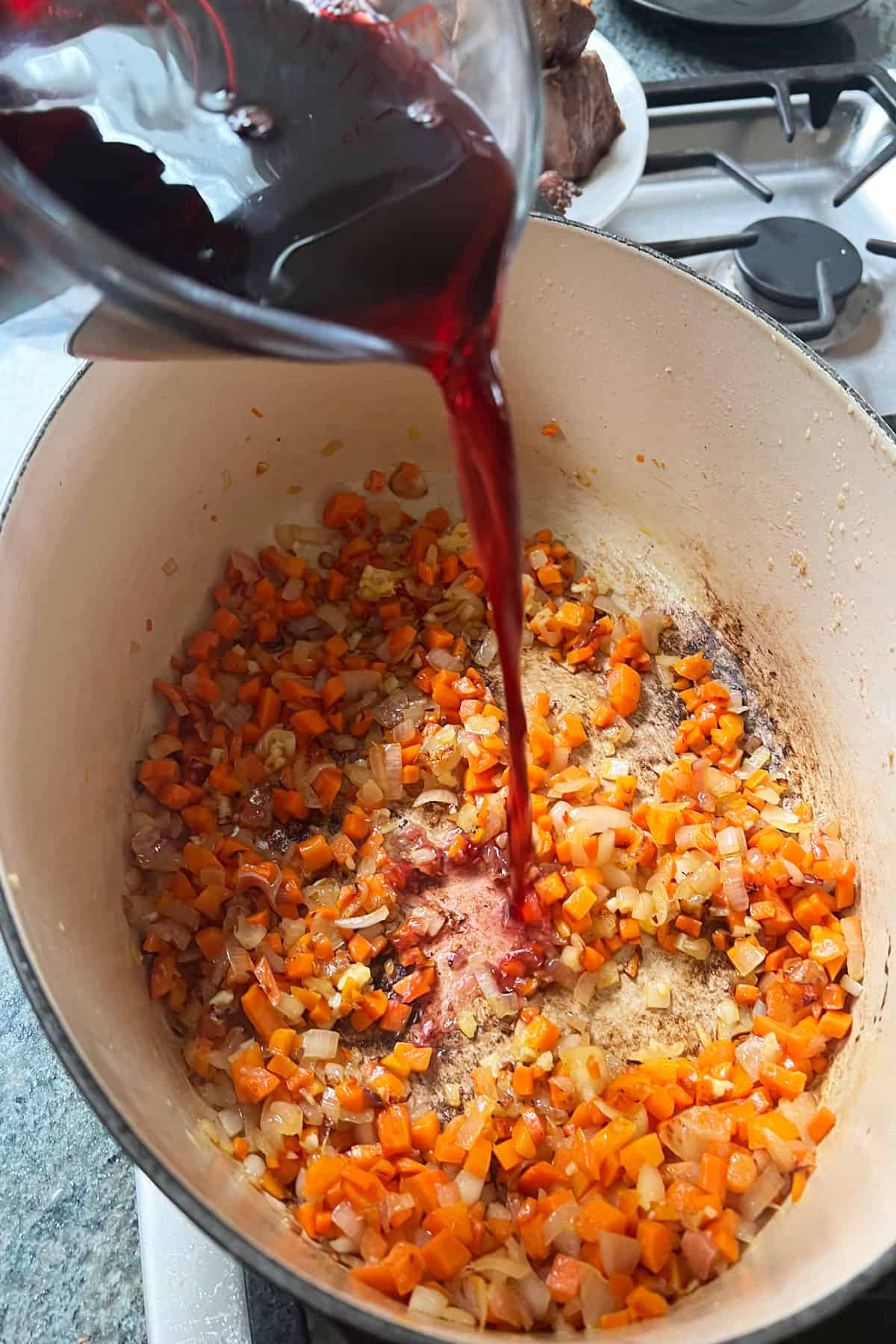 Red wine being poured from a measuring cup into the stew pot.