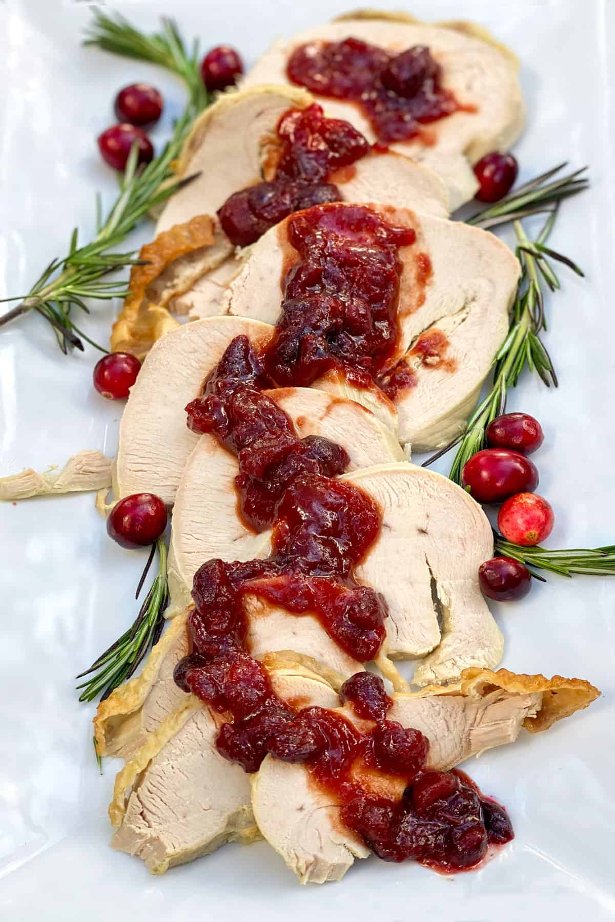 Platter of sliced roasted turkey topped with cranberry bourbon bbq sauce, with rosemary sprigs and fresh cranberries on the sides.